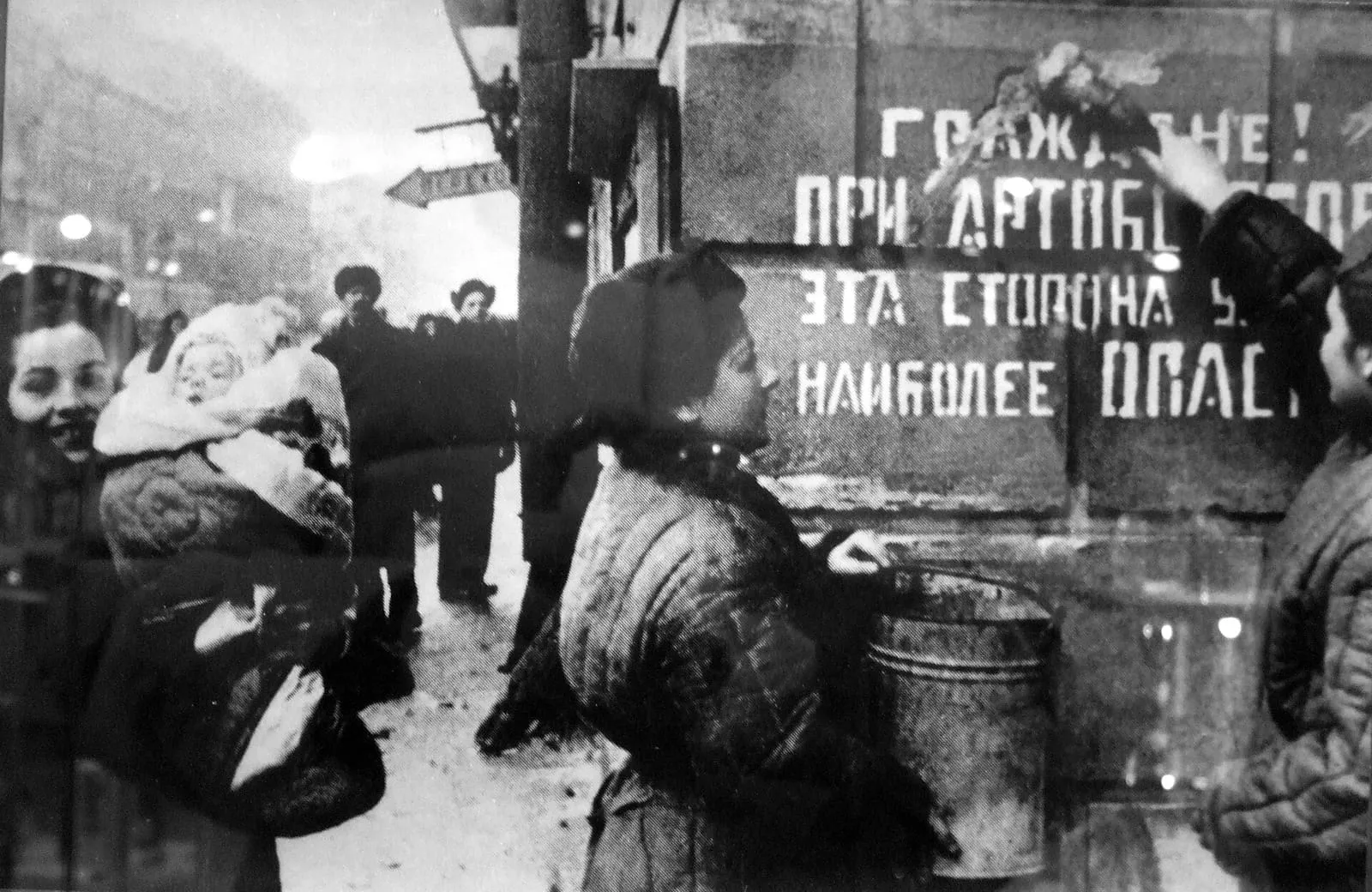 Leningraders beside a wall bearing a sign warning of artillery fire in the street, 1944.