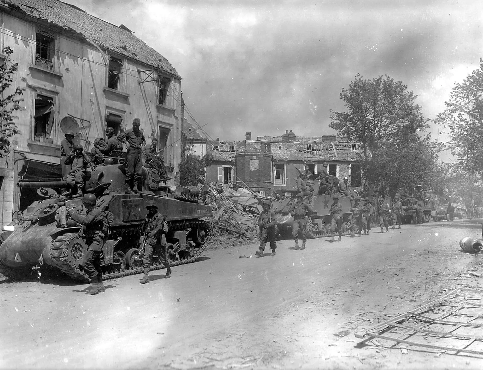 American armoured and infantry forces passing through the battered town of Coutances in July 1944.